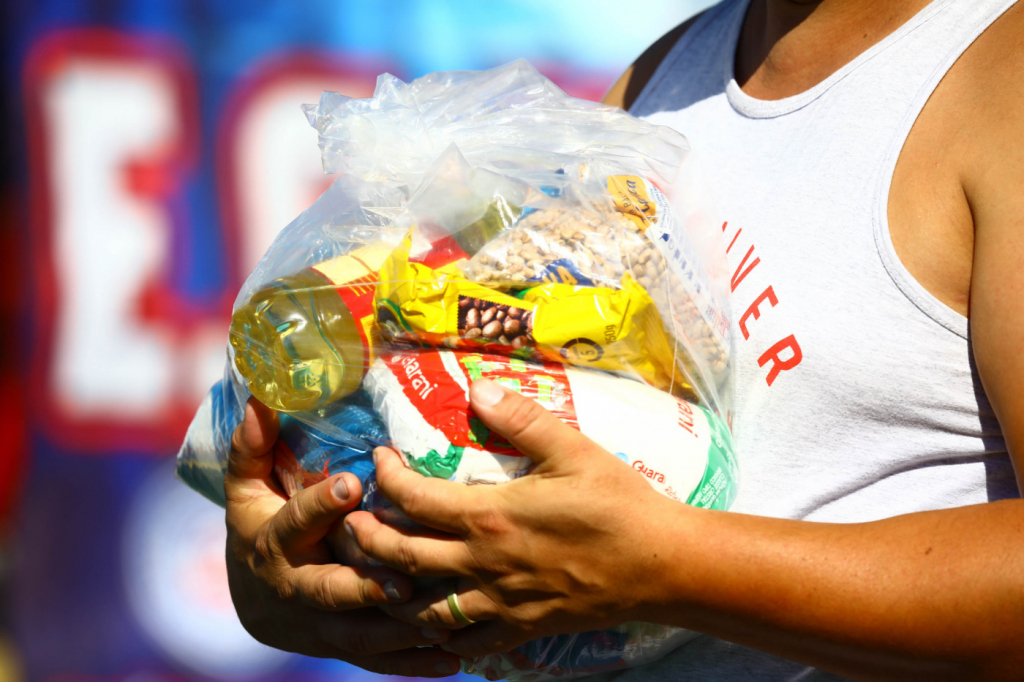 pessoa segurando em seus braços cesta básica cheia de gêneros alimentícios